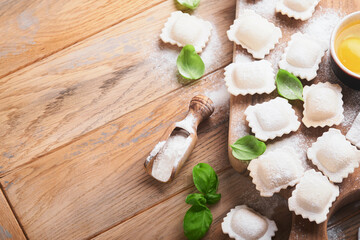 Obraz na płótnie Canvas Ravioli Italian food. Tasty homemade pasta ravioli with flour, tomatoes, eggs and greens basil on wooden background. Process of making italian ravioli. Food cooking ingredients background. Top view.