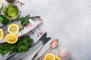 Fresh fish. Sea Bass raw with salt, pepper, parsley, olive oil and lemon on cutting board on light gray concrete rustic background. Food cooking background. Top view, copy space.