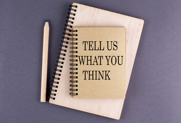 Word TELL US WHAT YOU THINK on notebook with pencil on the grey background