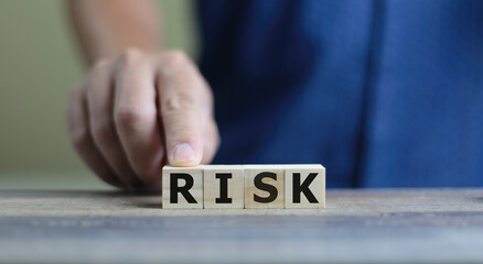 finger on  wooden cube block with  RISK word written on wood block, business concept.