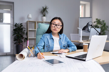 Portrait of young designer woman in modern office at work, successful Asian woman in glasses...