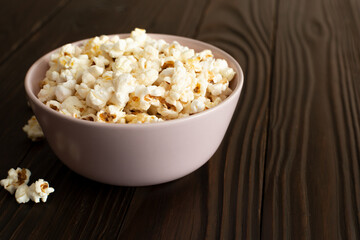 Bowl with popcorn on dark wooden table with copy-space