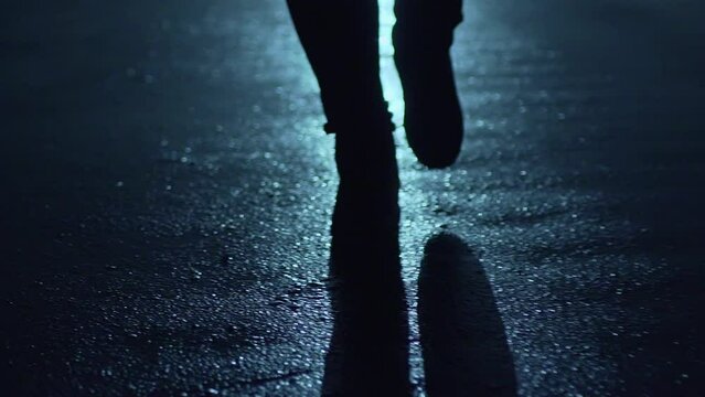 Legs of a man in backlight walking down the street at night.