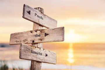 Fototapeta push the limits text quote on wooden crossroad signpost outdoors on beach with pink pastel sunset colors. Romantic theme. obraz