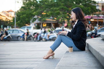 Fototapeta premium Asian businesswoman with laptop computer working outside looking at screens in the business district, professional women sitting outdoors