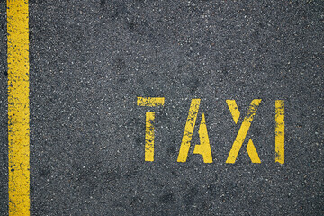 Yellow line and taxi sign on rough asphalt road in city..