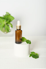 Fototapeta na wymiar Mock up glass dropper bottle on a white podium on a white background, with mint leaves. Cosmetic serum product on a white background. vertical with mint leaves