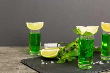 Sweet refreshing mint liqueur, with ice and mint leaves on table background, Shots with lime slice and mint flat lay