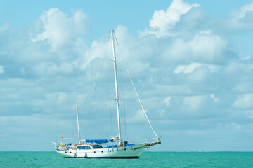 Single-deck white yacht on turquoise water. Sailboat with folded sail in the open sea in calm.