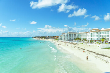 View of the Caribbean coastline. Sandy beach, blurry figures of tourists. Hotel buildings, palm trees. Panorama of the coast, Mexico.