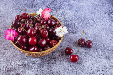 Fresh red cherries in a straw plate. Carnation flowers and berries lying on the table. Summer still life