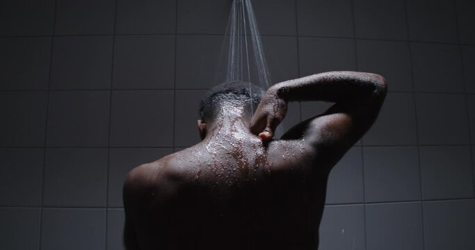 Young black male taking a warm steaming shower a in public shower room.