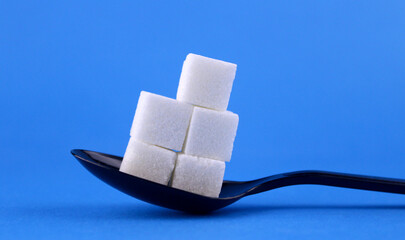 Obraz premium Sugar cubes in a black spoon on a blue background