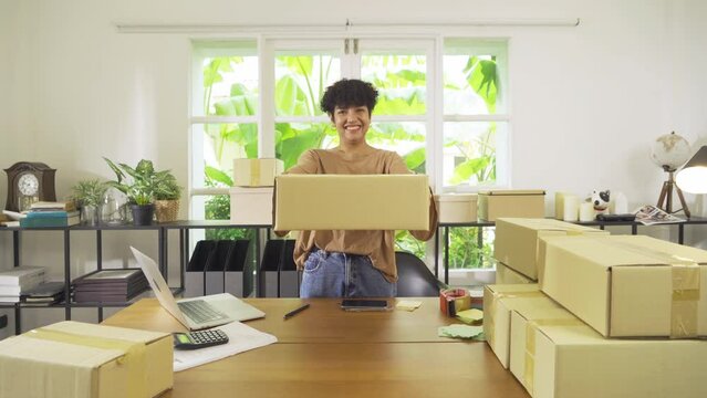 An Asian happy woman girl working online from home, selling product, packing postal parcel packaging carton box delivery, in social media. Online shopping business. SME ecommerce. People lifestyle.
