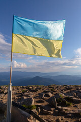 The flag of Ukraine flutters in the wind on top of a mountain in the Carpathians