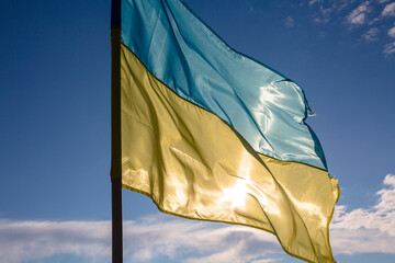 The flag of independent Ukraine is blowing in the wind against the blue sky and the setting sun