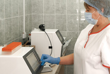 Woman scientist wearing face mask and protective gloves working in laboratory. Female researcher doing investigations using special blood test equipment with test tubes.