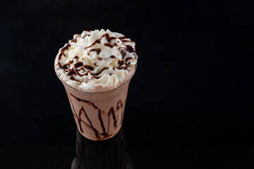 Chocolate milkshake served in a clear glass on a dark background. Isolated drink.