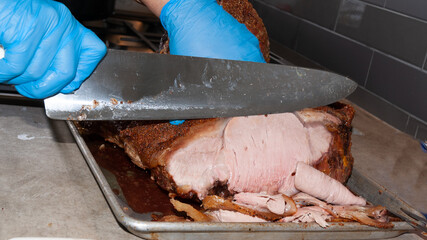 Trozo grande de roast beef cortada en filetes con cuchillo por manos con guantes de latex azul,...