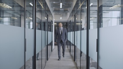 Successful businessman walking along office corridor with glass walls and doors