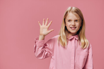 cute, beautiful, happy girl in pink clothes posing in the studio on a pink background showing five fingers and smiling broadly