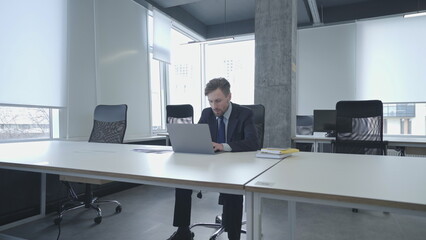 Concentrated businessman typing on laptop in large office, freespace for work