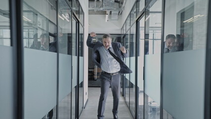 Excited businessman running in office corridor, jumping, happy with successful deal