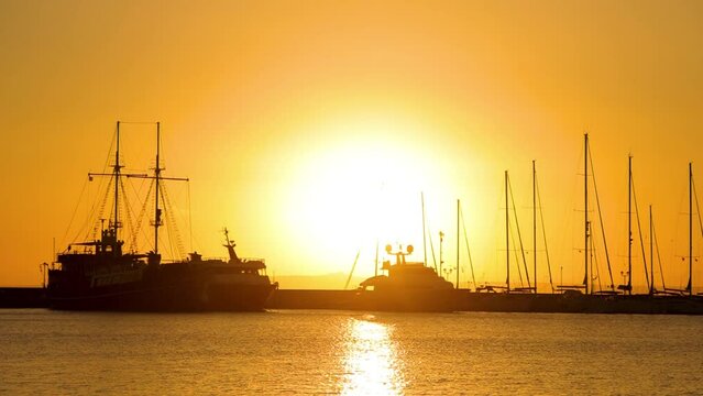 A huge sun, a jetty, harbor with big ship and yachts on the sunset background. 