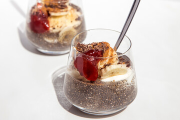 Chia seeds from the Salvia hispanica plant. Glass cup with hydrated seeds, natural yogurt, banana, strawberry jam, cinnamon powder and chocolate shavings. Image seen from above on white background.