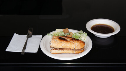 Sándwich de roast beef servido en un plato desechable con lechuga al lado y salsa de soya en un plato separado con fondo negro y servilleta y tenedor a un lado