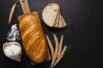 Fresh wheaten baton bread and flour on dark background.Top view. Copy space
