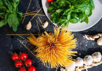 Ingredients for cooking pasta - raw spaghetti, basil, cherry tomatoes, garlic on a dark background. Top view. Italian cuisine concept
