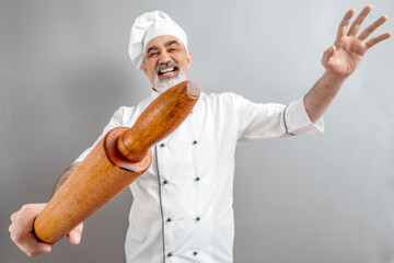 Chef-cooker in a chef's hat and jacket with wood rolling pin. Senior angry baker man wearing a chef's outfit. Character kitchener, pastry chef for advertising