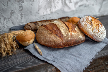 Homemade freshly baked bread, buns and a long loaf in a large wicker basket. Wood rustic table, board, ears, wheat, rye, grain harvest. Rural food cooking