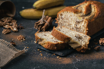 Fresh banana pie cut pieces on a black concrete background next to bananas and walnuts. Homemade pastry concept.
