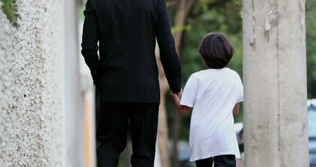 Father holding hands with child boy walking on city sidewalk