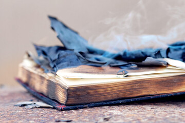 An open book with burnt charred pages and smoke on the table. Burning of banned literature
