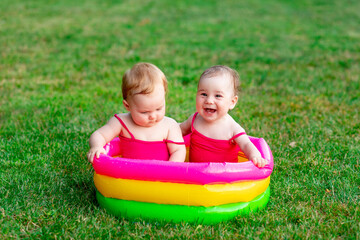 two children of joyful twins swim in an inflatable pool in the summer on the green grass, a space for text