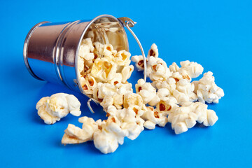 Small bucket filled with popcorn on a blue background.