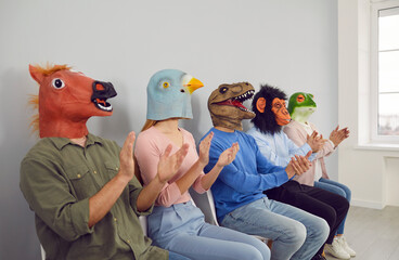 Diverse young people employees in funny animals rubber head masks sit in line clap hands show...