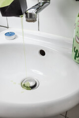 water and green liquid flowing into a small white sink (selective focus)