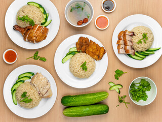 Chicken Cutlet and Roast Pork Rice, Roast Pork, Roasted Chicken, Roast Pork, Steamed Chicken with raw cucumber, Coriander, salad, sauce and soup served in a dish isolated on wooden background top view