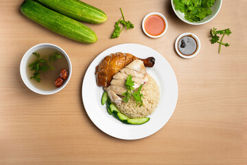 Steamed and Roasted Chicken Rice with raw cucumber, Coriander, salad, sauce and soup served in a dish isolated on wooden background top view