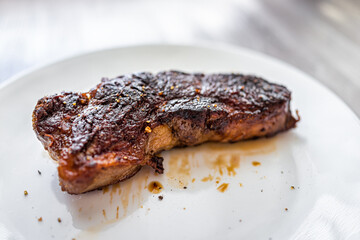 Medium rare grilled cooked grass-fed New York strip or ribeye meat beef steak on white plate serving
