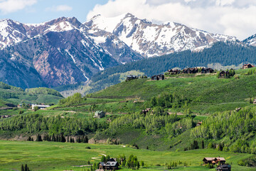 Mount Crested Butte town ski resort village mountain peak in summer with lodging houses on hills and green grass open valley and snowcapped rocky mountains