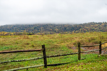 Virginia rural countryside farm cloudy mist fog day with wooden traditional fence by agricultural field in springtime or fall autumn with fallen dry brown leaves