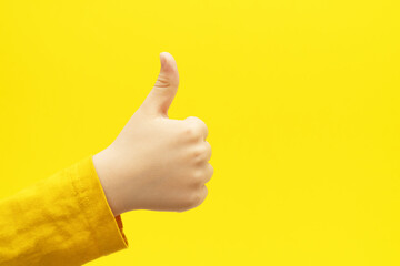 Child hand with thumb up gesture on bright yellow background. Like sign.