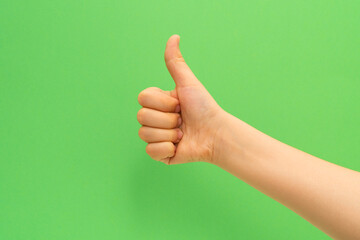 Child hand with thumb up sign on green background.
