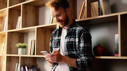 Portrait of attractive young man in the library hold smartphone, watching social media. Smiling young man texting on his phone.  - Powered by Adobe