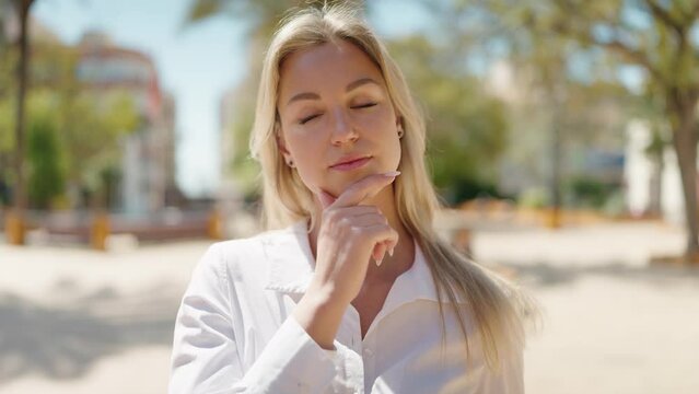 Young blonde woman standing with doubt expression at park